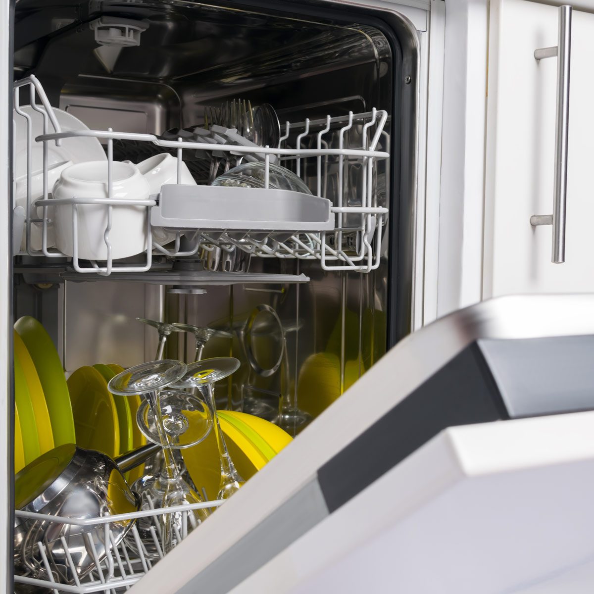 A dishwasher is open, filled with clean dishes, glasses, and utensils, arranged neatly in its wire racks, showcasing a mix of silver and bright yellow items.
