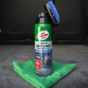 A green Turtle Wax cleaner stands upright on a green microfiber cloth, designed for deep cleaning carpets and mats in an indoor setting.