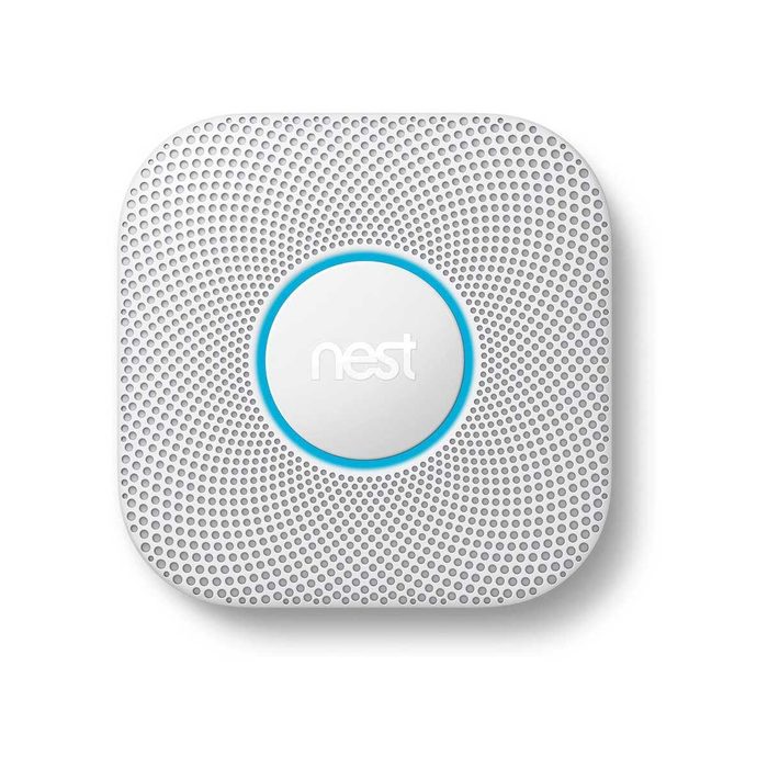 A white smoke detector with a circular design and ventilation holes is mounted on a flat surface, serving as a safety device in a home environment.