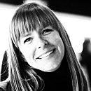 A woman with long hair smiles warmly, conveying joy in a soft-focus background, suggesting a friendly and inviting atmosphere.