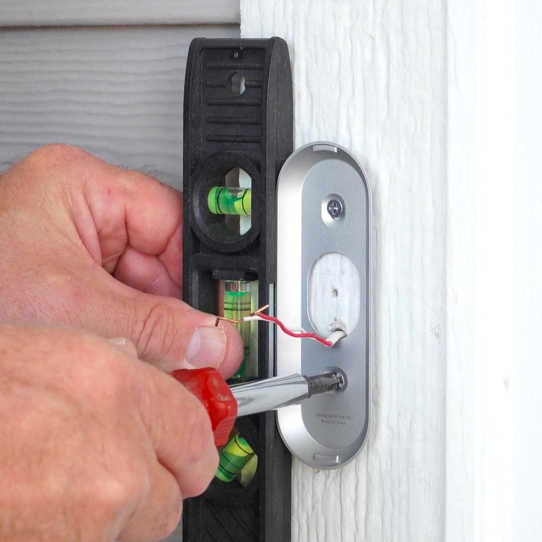 A hand uses a screwdriver to install a silver device on a white wall, while a level nearby ensures it is even.