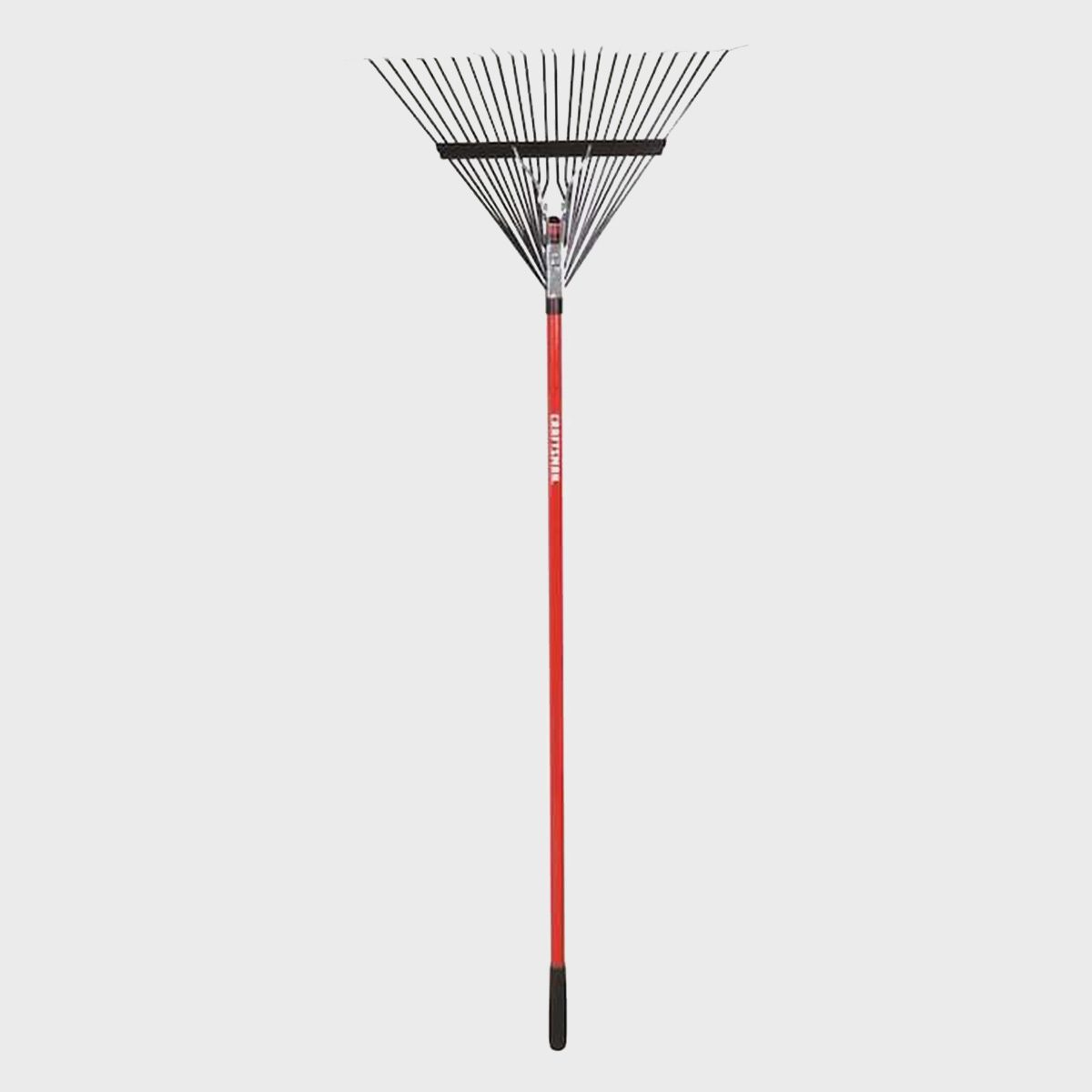 A red rake stands upright, its wide head featuring multiple thin tines, used for gathering leaves or debris in garden or yard settings.