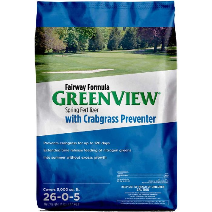 A bag of GreenView spring fertilizer prevents crabgrass, offers nitrogen feeding, and covers 5,000 square feet, set against a green lawn background.