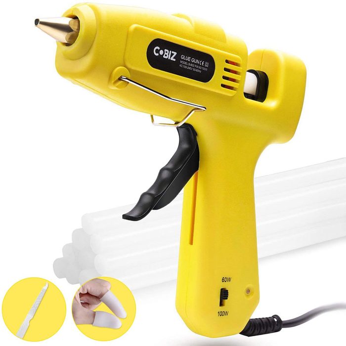 A yellow glue gun dispenses adhesive from its nozzle, positioned alongside several glue sticks, suggesting use in crafting or repairs.