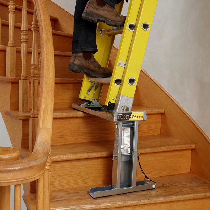 A yellow ladder rests on a stair aid device, with a person stepping on it near a wooden staircase.