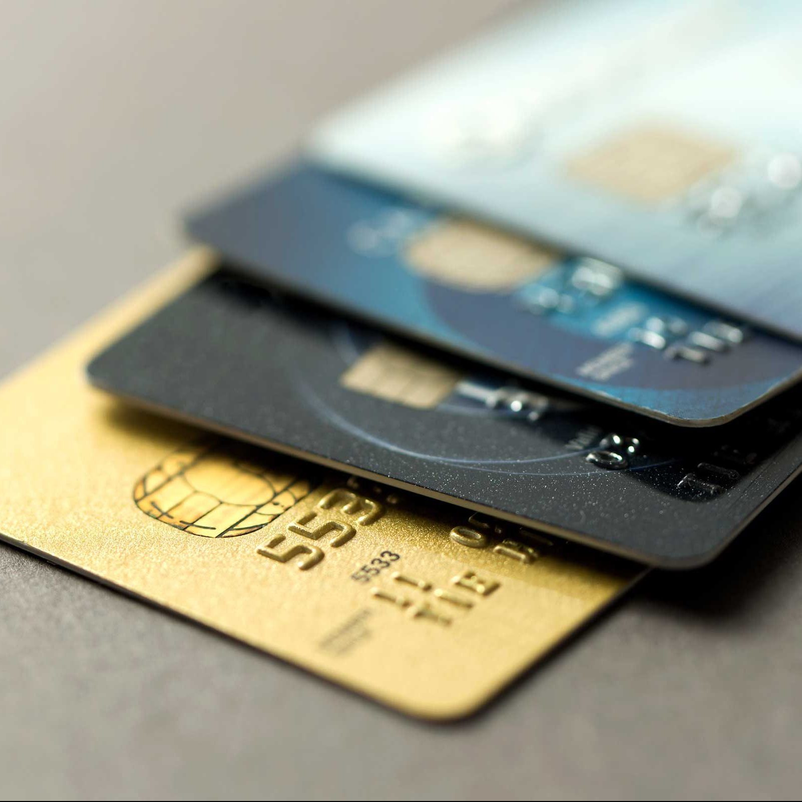Three credit cards are arranged in a stack, displaying various colors and designs, resting on a smooth surface.