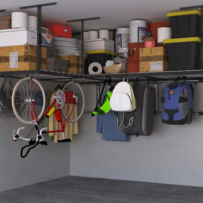A red bicycle hangs from a shelf, surrounded by stacked boxes and various storage containers, within a spacious garage environment.