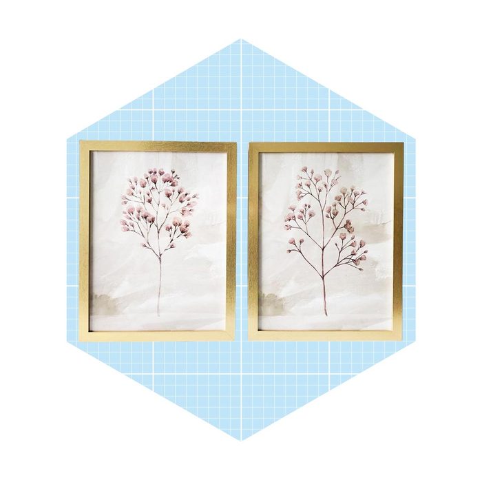 Two framed botanical illustrations display delicate pink branches against a soft background, set within a light blue, patterned context resembling a room