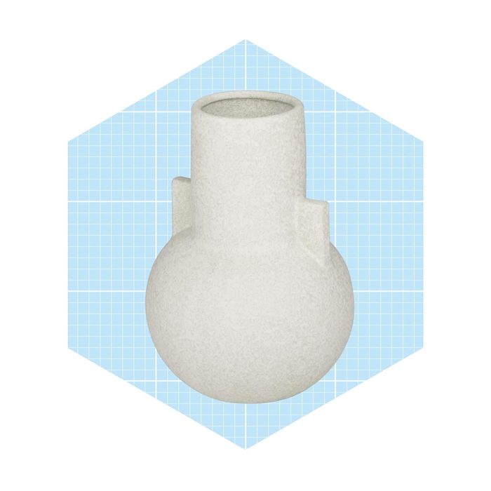 A textured, white ceramic vase stands upright against a light blue grid background. Its round body transitions into a narrow neck, giving it a modern design.