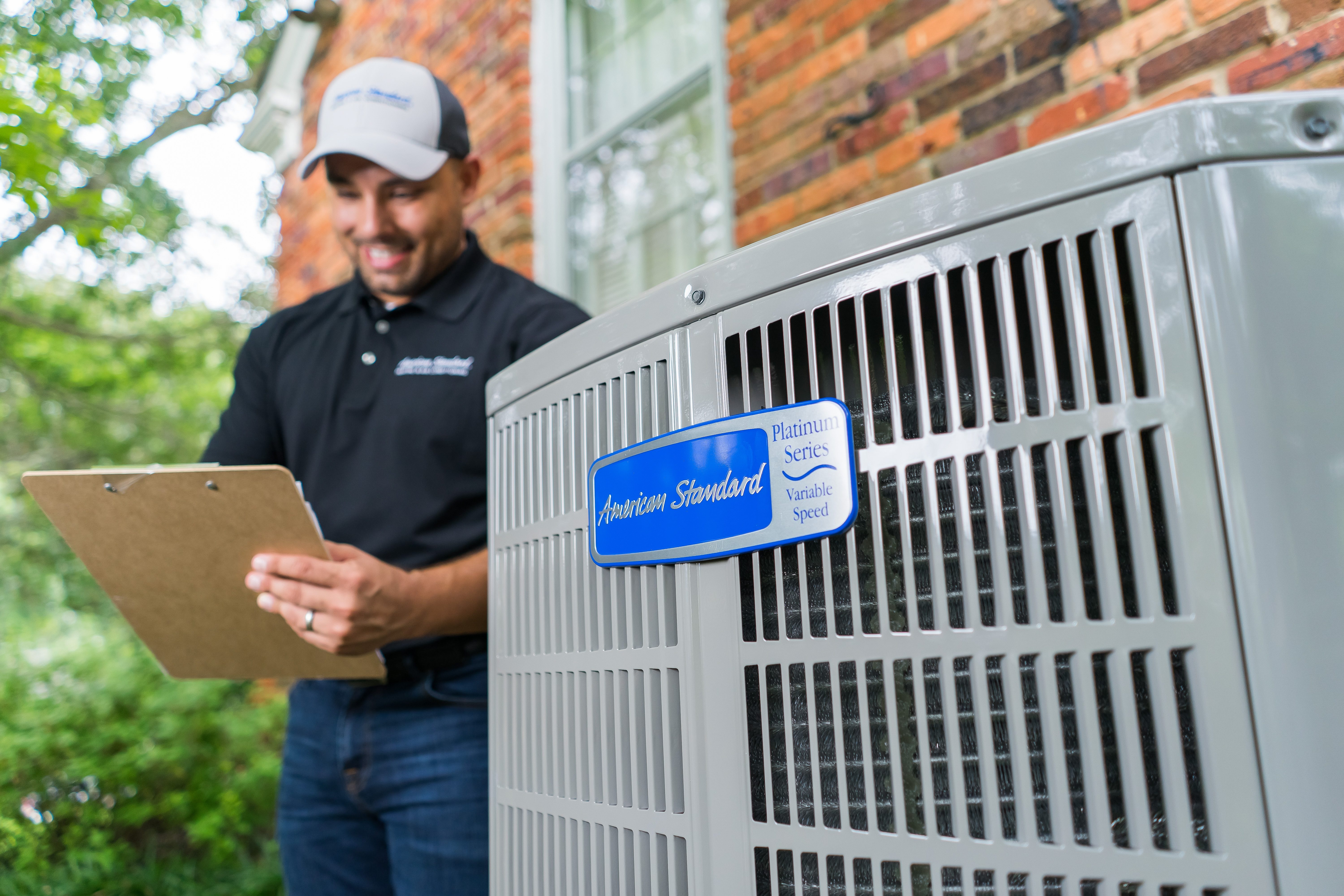Close up on logo of Platinum 20 Heat Pump / Air Conditioner placed outside while American Standard technician makes notes