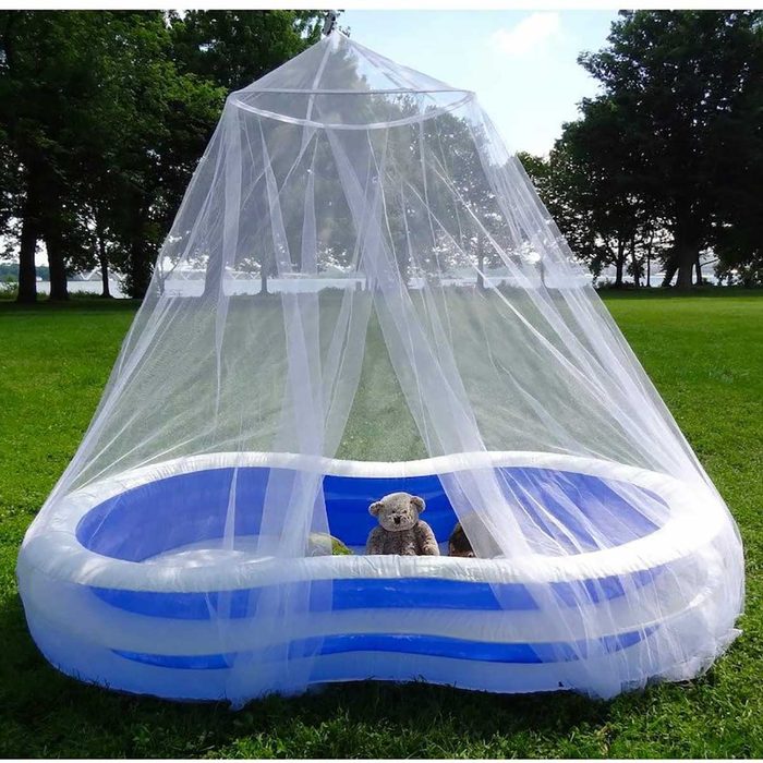 An inflatable pool is covered with a sheer canopy. Inside, a stuffed bear sits surrounded by greenery on a grassy area near trees.
