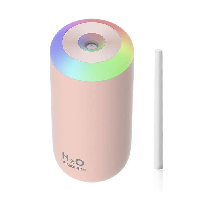 A cylindrical pink humidifier releases mist, with a colorful light ring atop. Beside it, a white straw-like component rests.