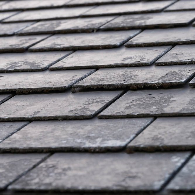 A close-up view of dark, textured roof shingles arranged in a staggered pattern, capturing the details of their weathered surface.