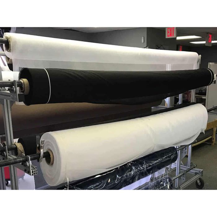 Rolled fabric in various colors rests on a display rack, showcasing white, black, and brown material in a well-lit indoor setting.
