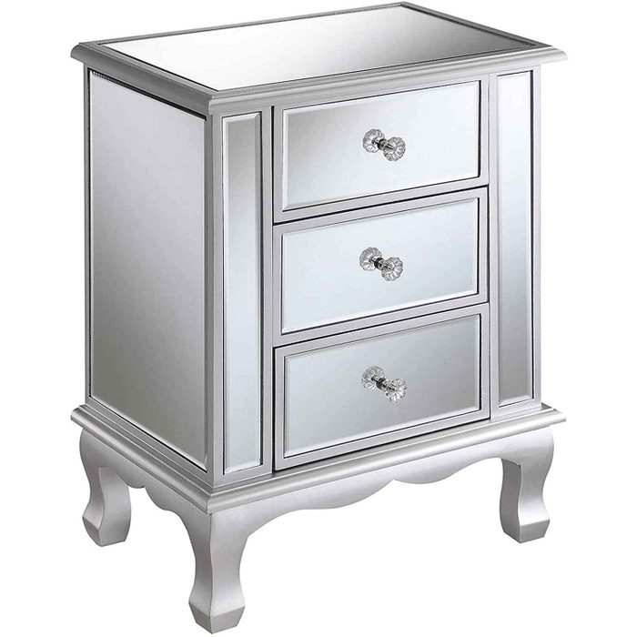 A mirrored nightstand stands with three drawers, showcasing reflective surfaces and crystal knobs, elegantly placed in a bright, modern room.