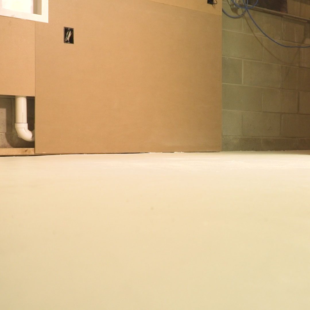 A smooth, light-colored floor stretches before a wall featuring a utility pipe and electrical outlets, in a minimally furnished, enclosed space.