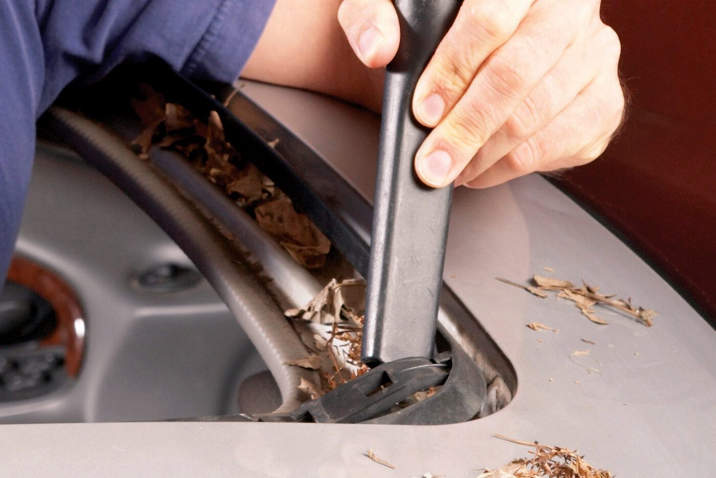 A person uses a tool to clean leaves from a car