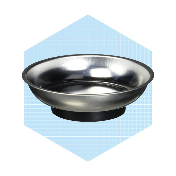 A metallic bowl sits on a black base, reflecting light, against a light blue grid background, emphasizing its smooth surface and round shape.