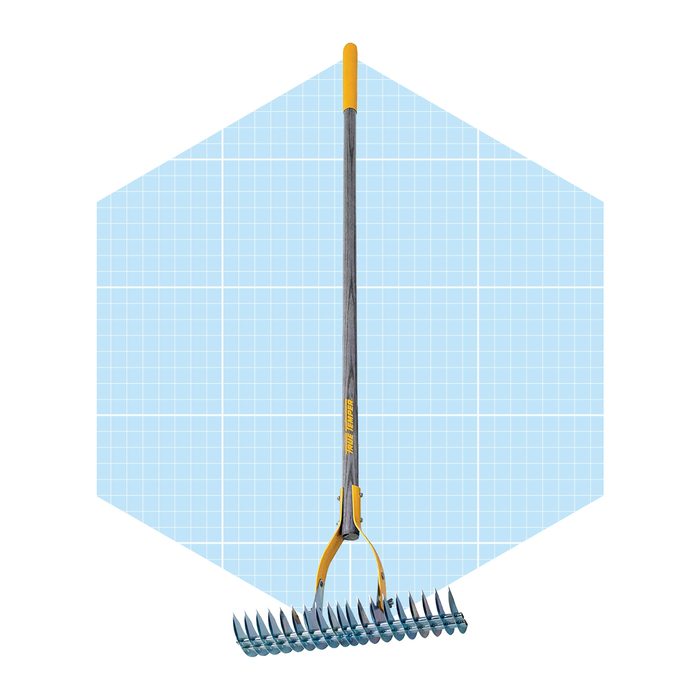 A metallic garden rake stands upright, its pronged head facing down, set against a light blue grid background.