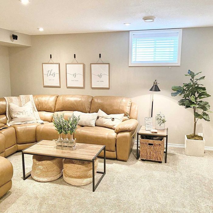 A leather sectional sofa sits in a cozy room, accompanied by a wooden coffee table, decorative pillows, and framed art on the wall. A plant adds greenery.