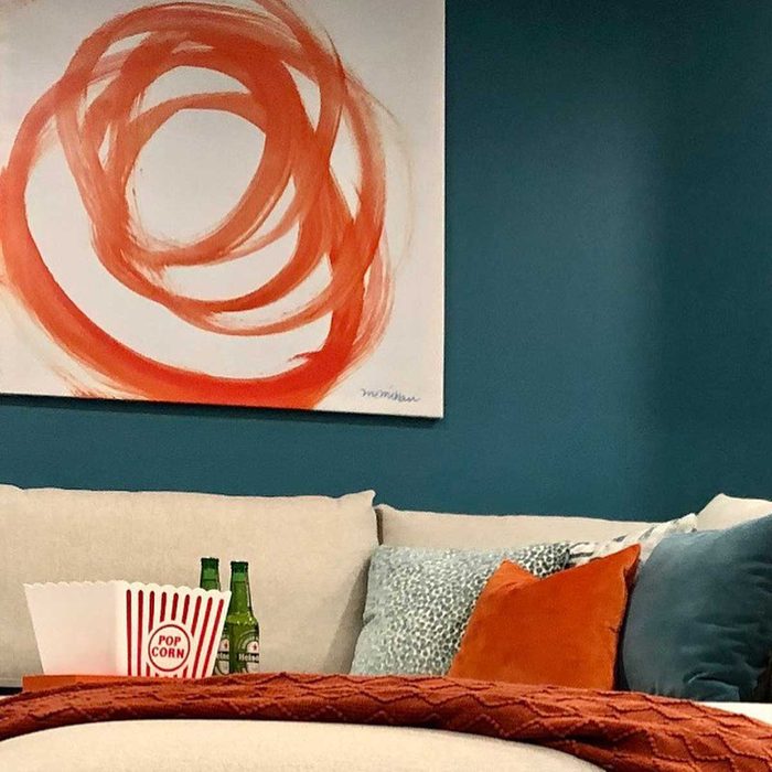 A sofa features colorful pillows and a cozy blanket. Nearby, a red-and-white popcorn container sits beside two green bottles on a wooden table against a blue wall.