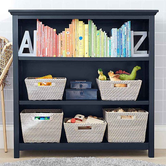 A dark bookshelf holds colorful books and baskets filled with toys in a bright, organized playroom environment.