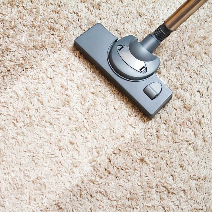 A vacuum cleaner rests on a light-colored, plush carpet, ready to clean. The environment suggests a home setting focused on maintaining cleanliness.