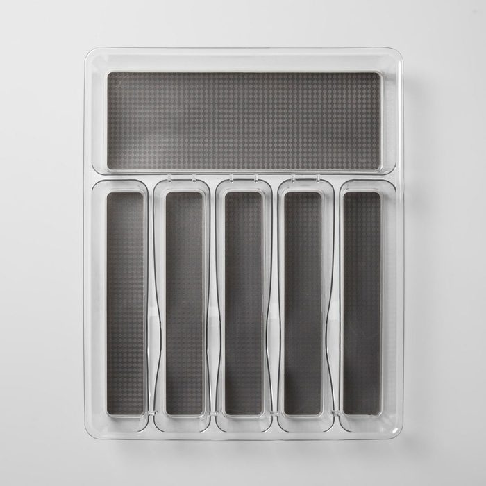 A transparent organizer with five elongated compartments and one larger section is designed for sorting small items, placed on a light-colored surface.