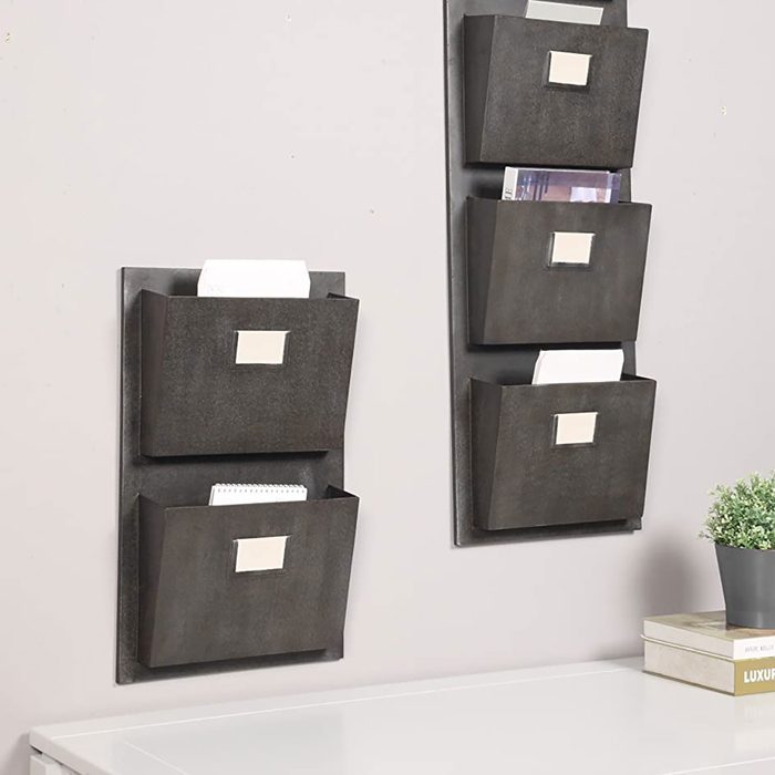 Wall-mounted organizers hold various papers, displaying labels. They are positioned above a surface with books and a small potted plant, enhancing organization.
