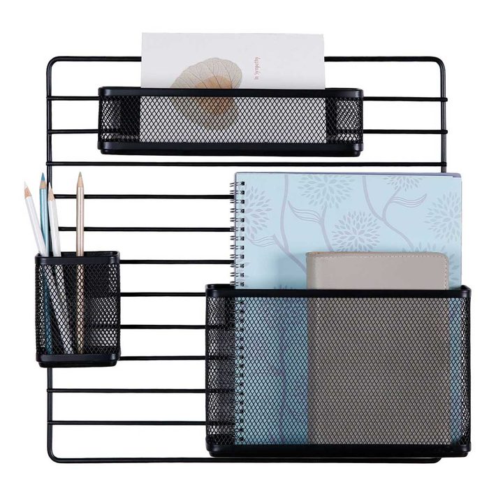 A black wire wall organizer holds notebooks, a planner, and writing utensils, offering structured storage in an office or study environment.