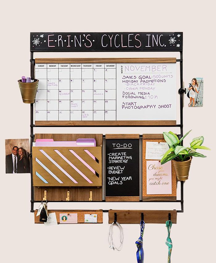 A wall-mounted organizational board displays a calendar, tasks, and notes. It holds folders, a plant, and personal photos, enhancing a workspace ambiance.