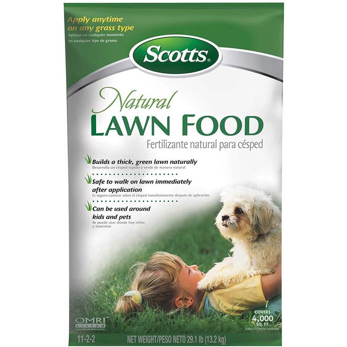 A bag of Scotts Natural Lawn Food rests, emphasizing lush lawn growth while a child interacts with a small dog, suggesting a family-friendly environment.