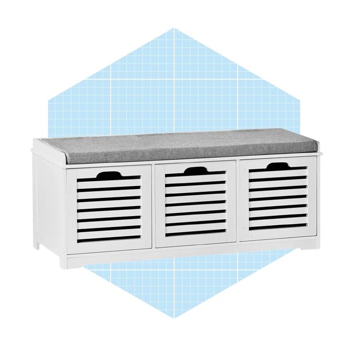 A white storage bench with a gray cushioned top sits against a light blue geometric background, featuring slatted doors for storage accessibility.