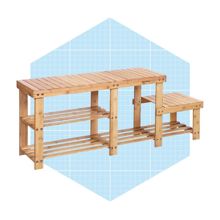 A wooden shelf unit stands with multiple levels for storage, featuring a shorter side section, set against a light blue geometric background.