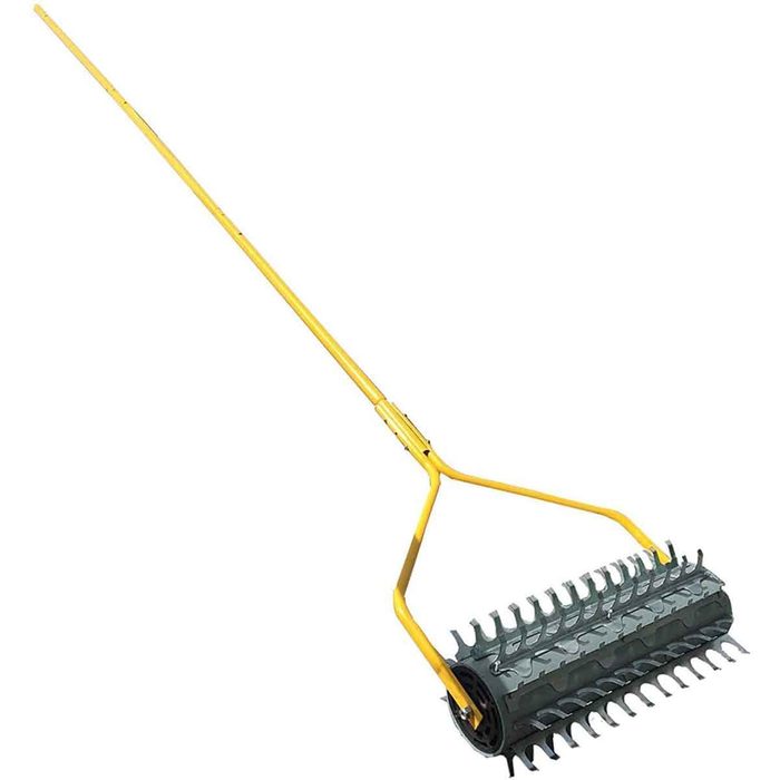 A lawn-leveling rake features a long yellow handle and a cylindrical roller with protruding spikes, used for leveling soil in a landscaping context.