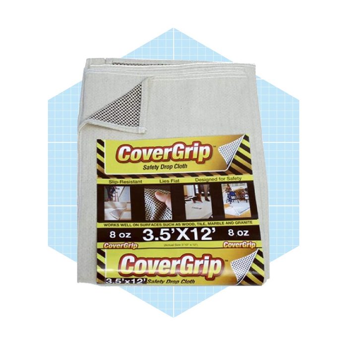 A safety drop cloth lies flat, designed to prevent slips. It is packaged prominently, showcasing features suitable for various surfaces like wood and tile.