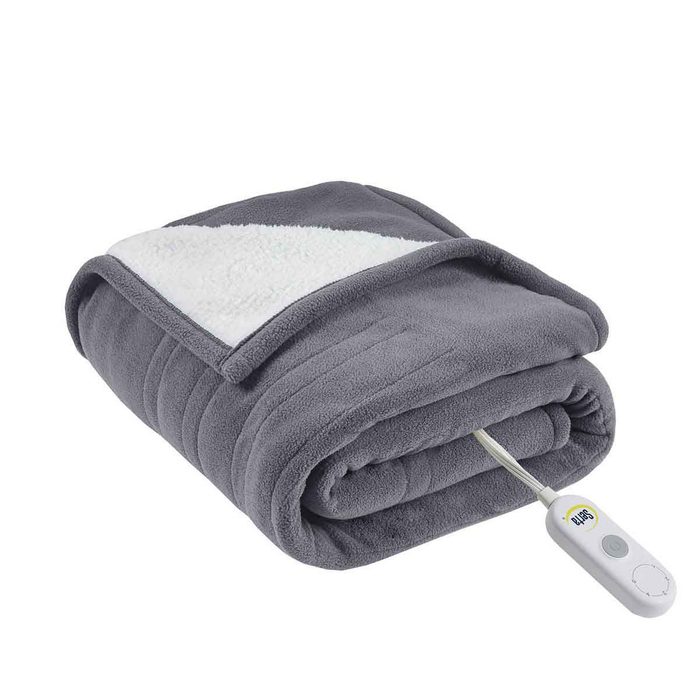 A gray electric blanket is neatly rolled up, showcasing its soft texture, with a white control remote attached, ready for use in a cozy setting.