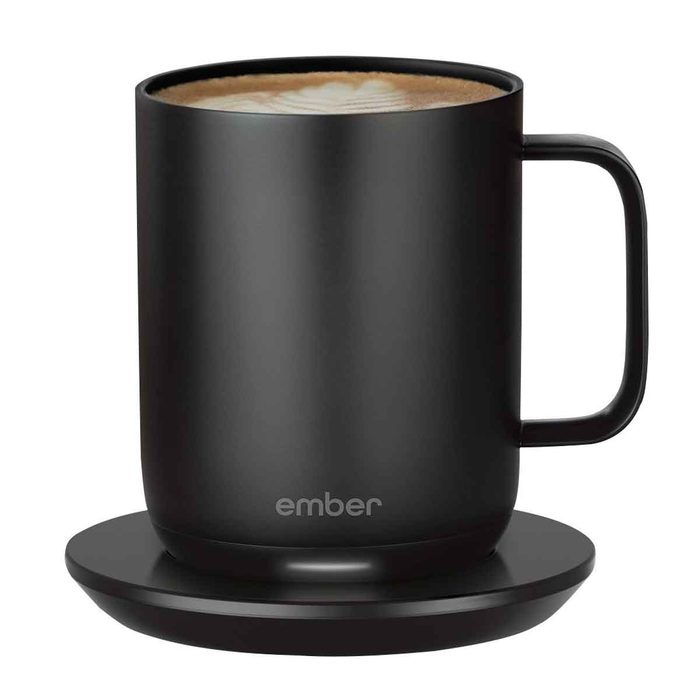 A black smart mug sits on a matching base, containing a creamy beverage, designed to maintain temperature with a sleek, modern appearance.