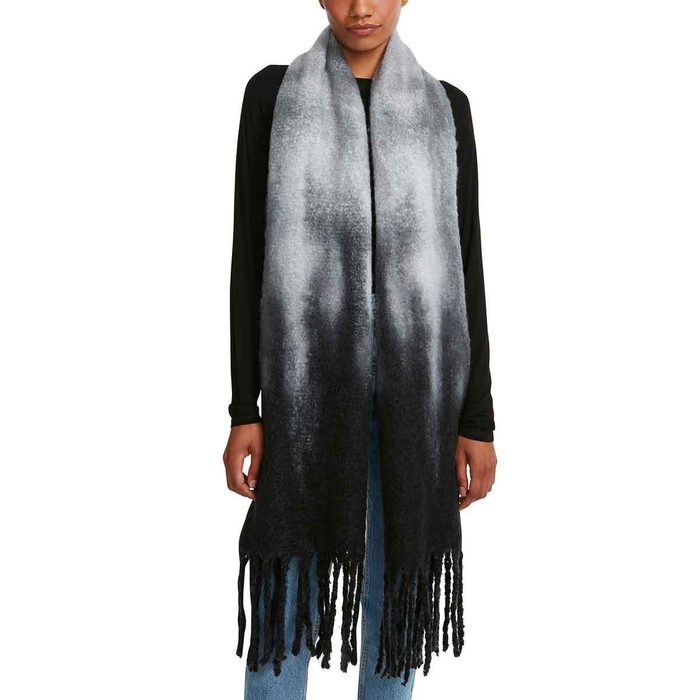 A woman wears a long, gradient scarf that transitions from gray to black, standing against a neutral background with her arms relaxed at her sides.