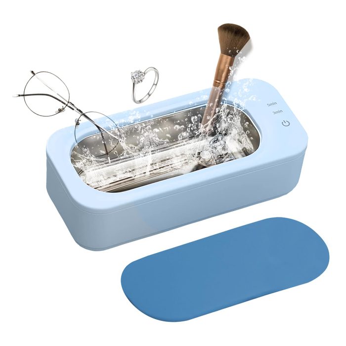 A blue ultrasonic cleaner holds eyeglasses, a ring, and a makeup brush, while water splashes inside, indicating active cleaning in a domestic setting.