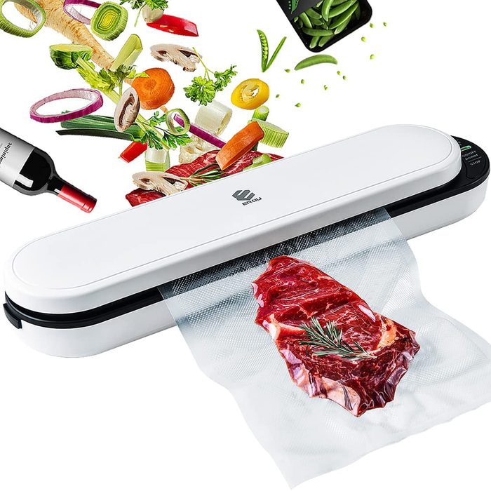 A vacuum sealer houses a raw steak enclosed in plastic, while assorted vegetables and a wine bottle hover above, suggesting preparation for a meal.