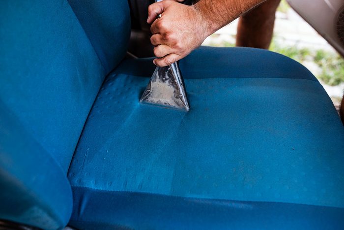 A hand holds a cleaning tool, removing dirt from a blue fabric chair cushion, situated in a casual outdoor setting.