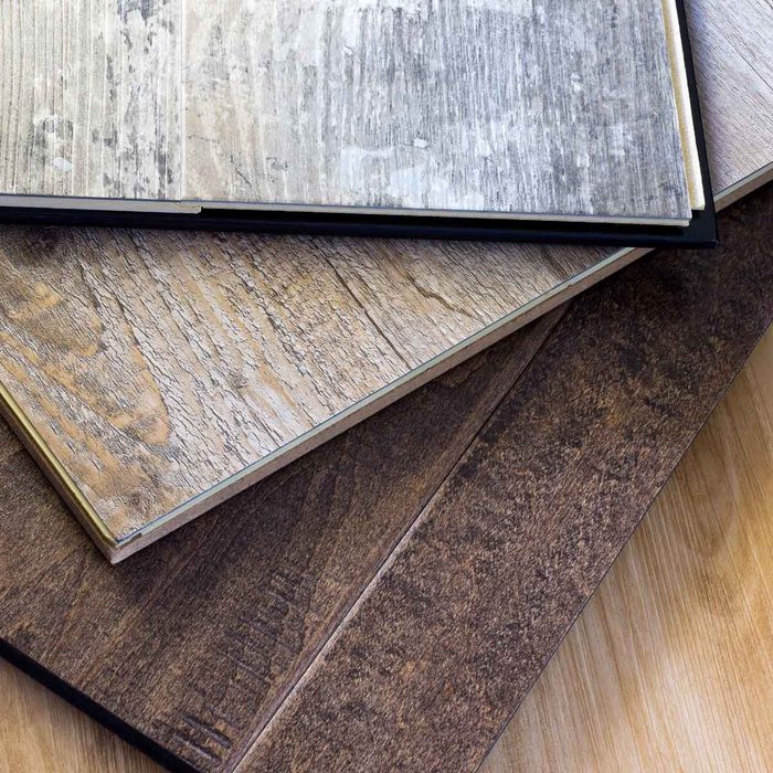 Several textured laminate flooring samples are stacked, showcasing varying wood grain designs, with a light wooden surface below them indicating a display or selection area.
