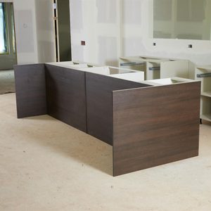 A wooden counter is positioned in an unfinished room, with partial cabinetry in the background and bare walls, indicating an ongoing construction or renovation.