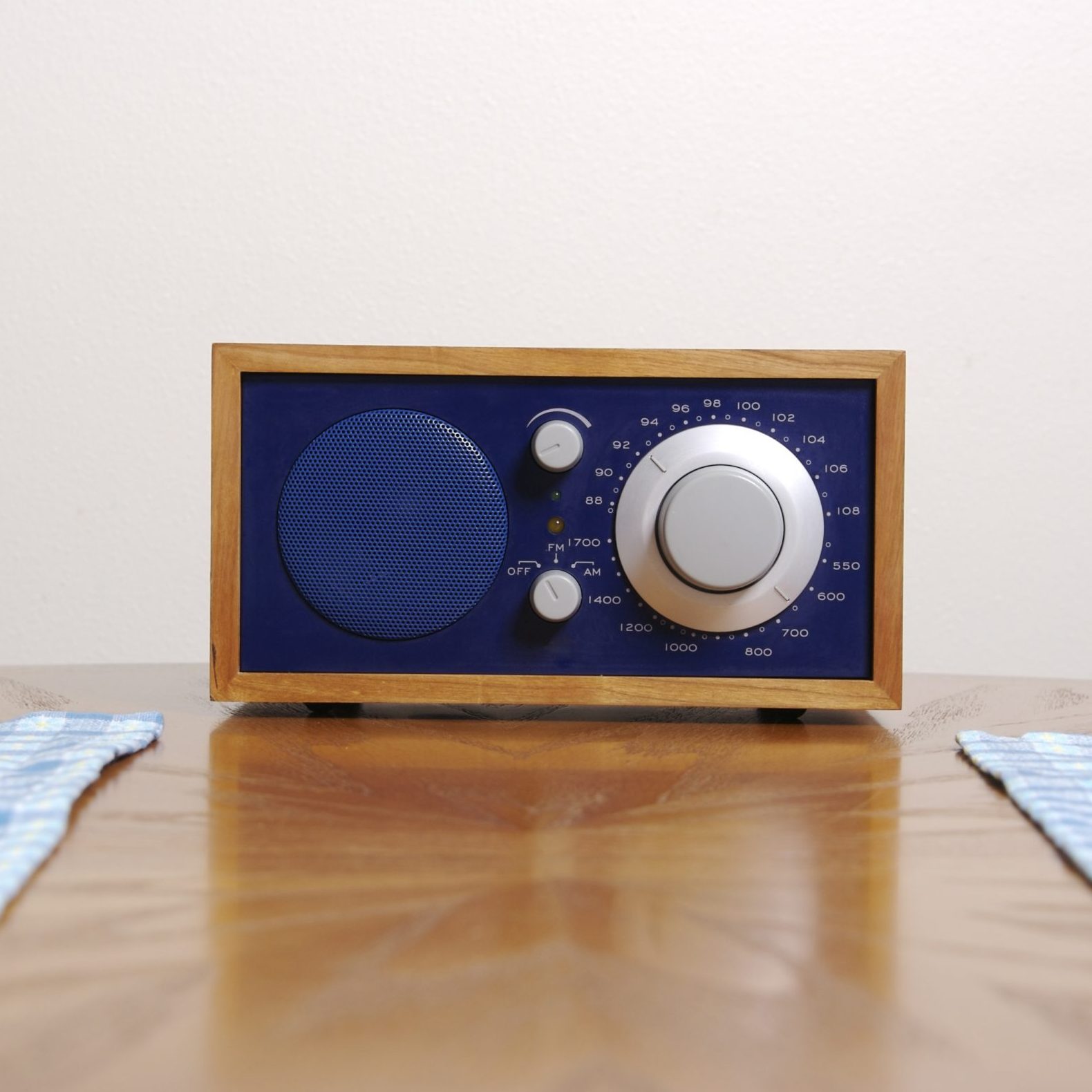 A blue and wooden radio sits on a table, featuring a large tuning knob and a speaker, set against a plain wall.