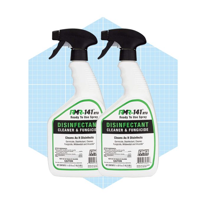 Two white spray bottles with black nozzles contain a disinfectant cleaner. They are positioned against a light blue grid background.