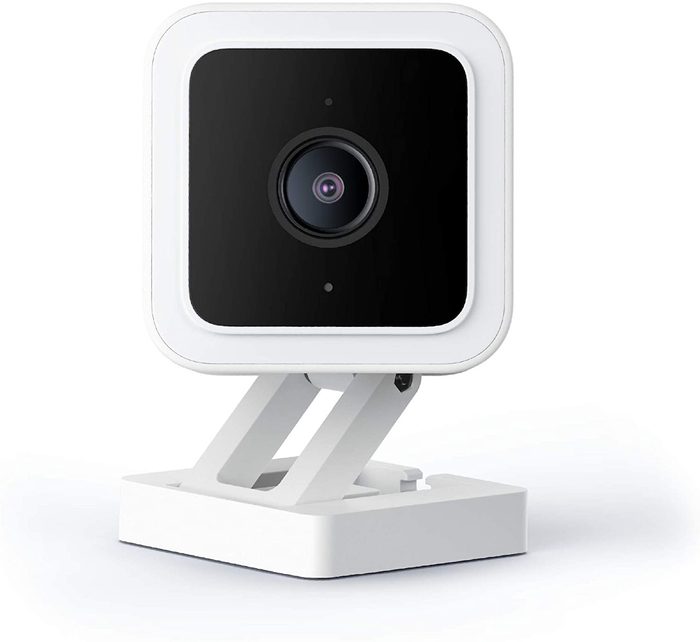 A square camera with a black lens is mounted on a white adjustable stand, positioned on a flat surface, likely for monitoring or recording.