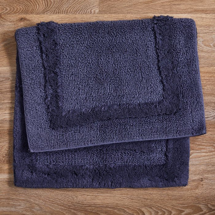 Two dark gray towels are stacked neatly on a wooden surface, showcasing their textured fabric and bordered edges.