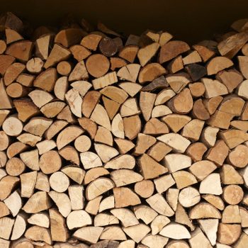 Stacked firewood fills a space, consisting of various sizes of cut logs, arranged neatly against a dark background.