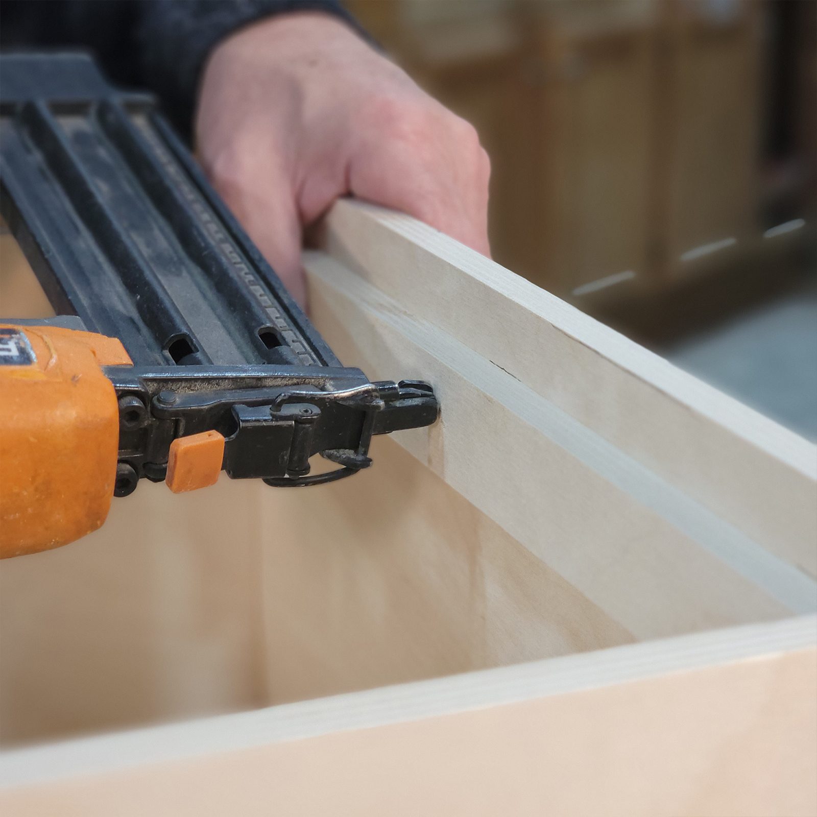 A person uses a nail gun to fasten two pieces of wooden boards together in a workshop, demonstrating a woodworking technique.